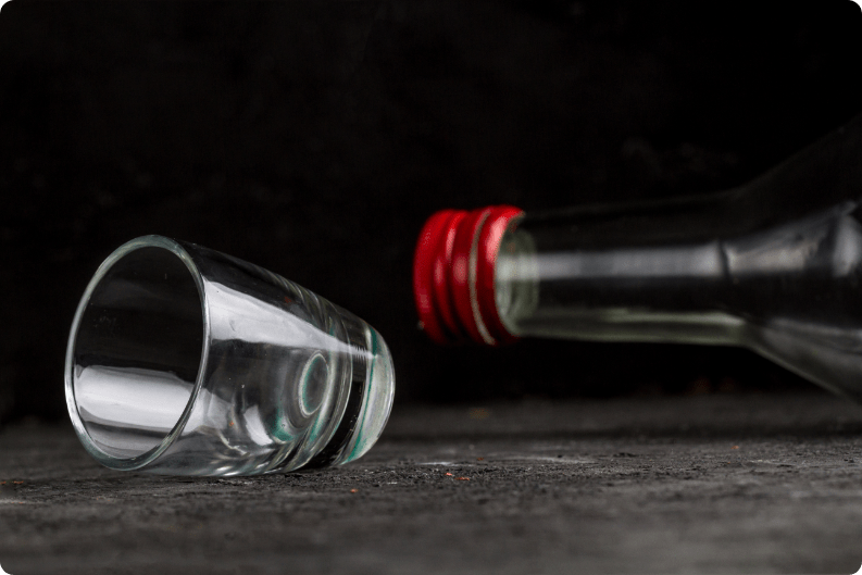 Ekranda devrilmiş kırmızı kapaklı bir alkol şişesi ve shot bardağı duruyor. 